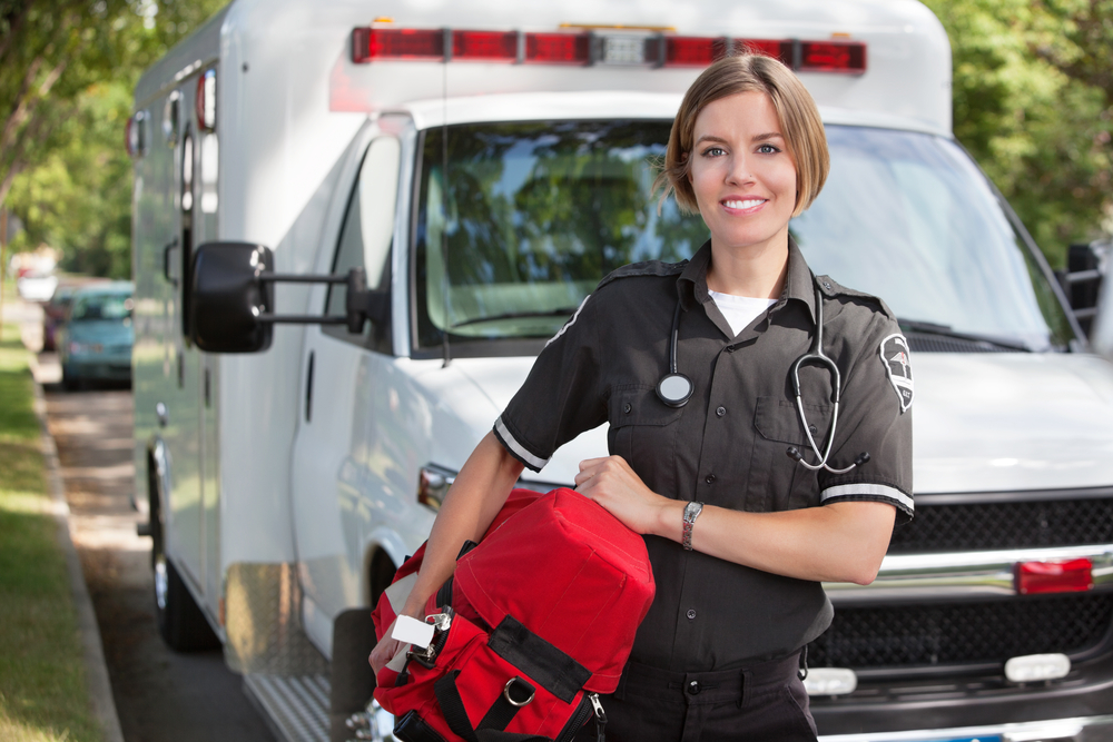 First Responder holding a portable oxygen unit smiling in front of an emergency vehicle