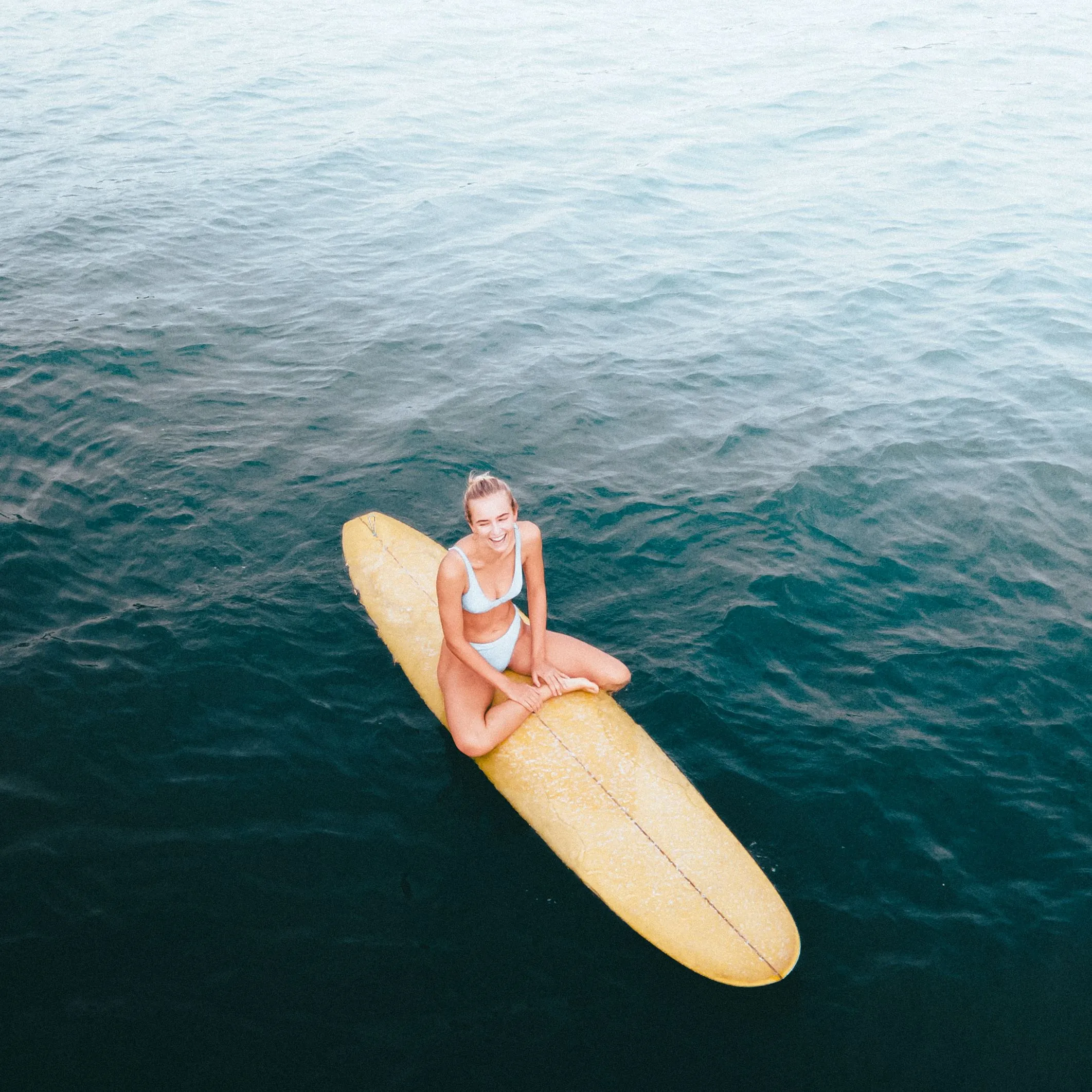 Active woman smiling while sitting on a surfboard, representing healthy living supported by Alpha-Lipoic Acid IM antioxidant and cellular energy therapy.